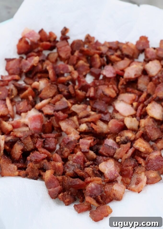 Crispy diced cooked bacon resting on a paper towel-lined plate to drain excess grease.