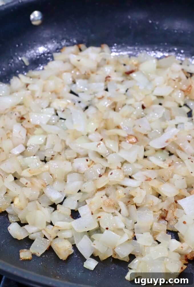 Diced onions cooking and caramelizing in a skillet with a tablespoon of reserved bacon drippings.
