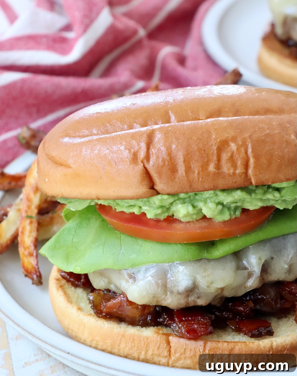 A delicious California burger served on a plate with crispy truffle fries, showcasing a juicy patty, melted white cheddar, fresh avocado, and savory bacon jam, ready to be enjoyed.
