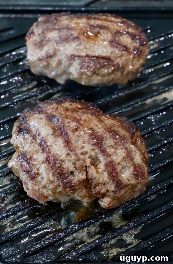 Juicy burger patties sizzling on a hot grill pan, showing an excellent sear and beginning to cook through, capturing the essence of outdoor grilling.