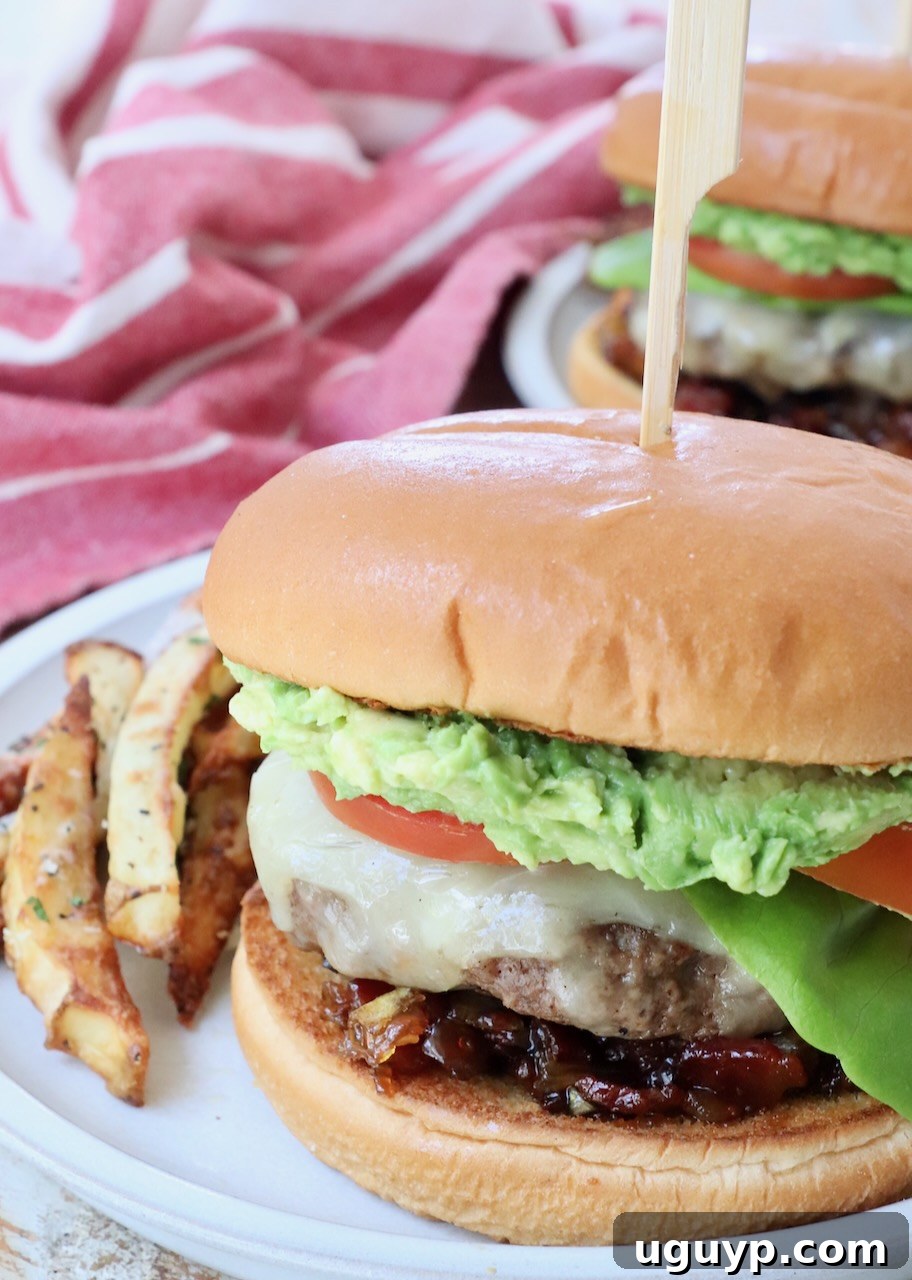 A perfectly assembled California burger on a plate, surrounded by golden, crispy truffle fries, showcasing its vibrant layers of fresh ingredients and gourmet appeal.
