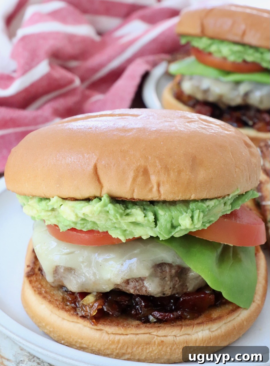 A vibrant close-up of a California burger served on a plate, featuring a thick, juicy patty, melted cheese, and a generous layer of smashed avocado, topped with fresh lettuce and a ripe tomato slice.