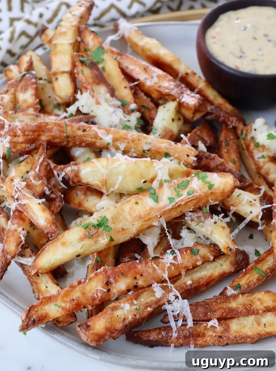 Crispy parmesan truffle fries on a plate with a small bowl of dipping sauce on the side, ready to be enjoyed.