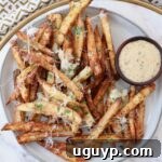 Cooked fries on plate topped with Parmesan cheese and parsley, with small bowl of sauce on the side.