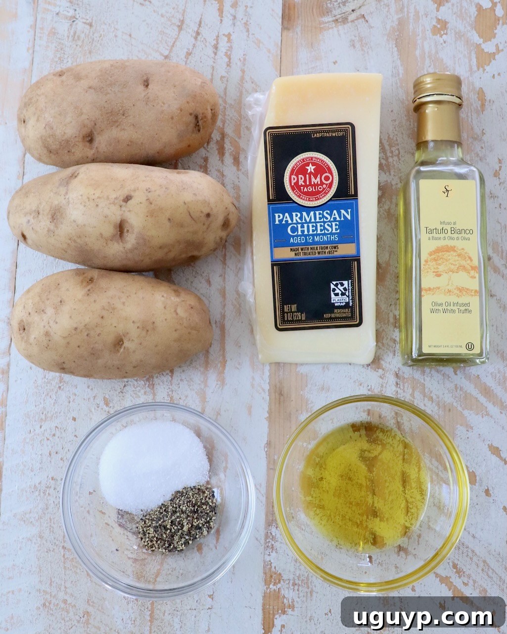 Assortment of fresh ingredients for truffle fries laid out on a white wooden board, including potatoes, olive oil, truffle oil, Parmesan, and parsley.