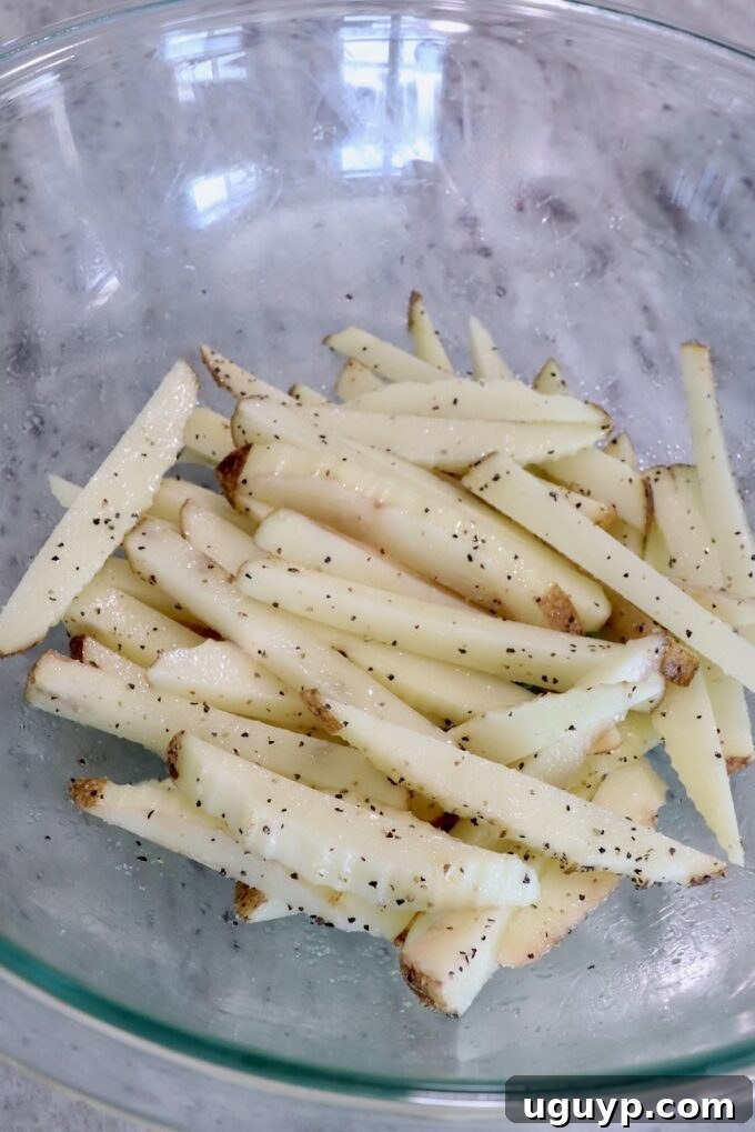 Seasoned, hand-cut potatoes arranged as french fries in a clear glass bowl, ready for cooking.