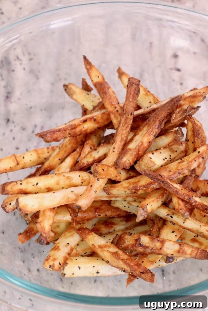 Perfectly cooked, crispy french fries gathered in a glass bowl, waiting for their truffle and Parmesan seasoning.