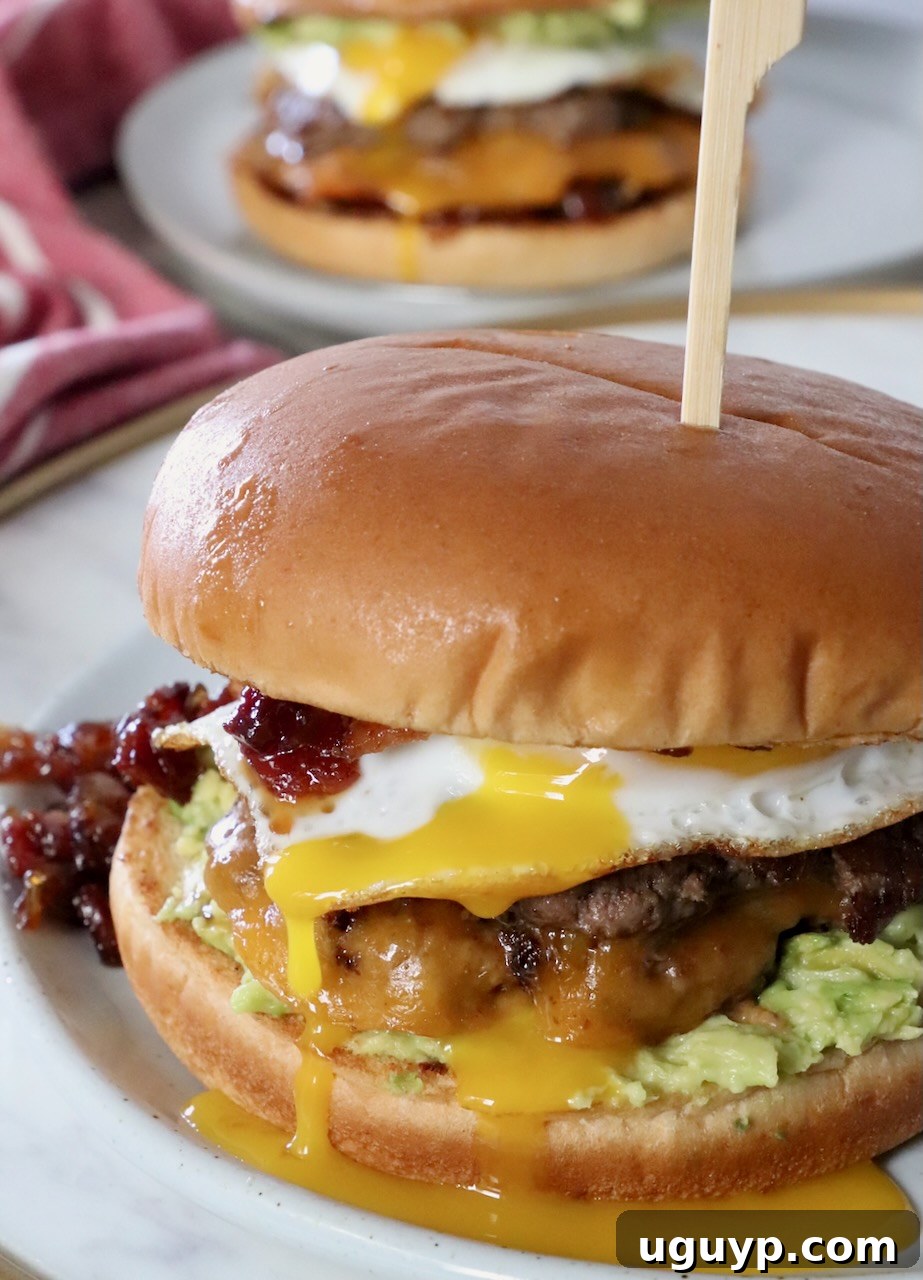 A gourmet breakfast burger on a plate with egg yolk gently dripping down, showcasing its mouth-watering appeal.