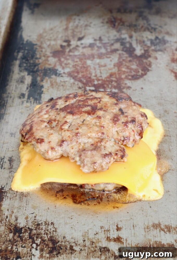Two burger patties stacked on top of each other with a slice of melted cheese in between, still on the flat top.