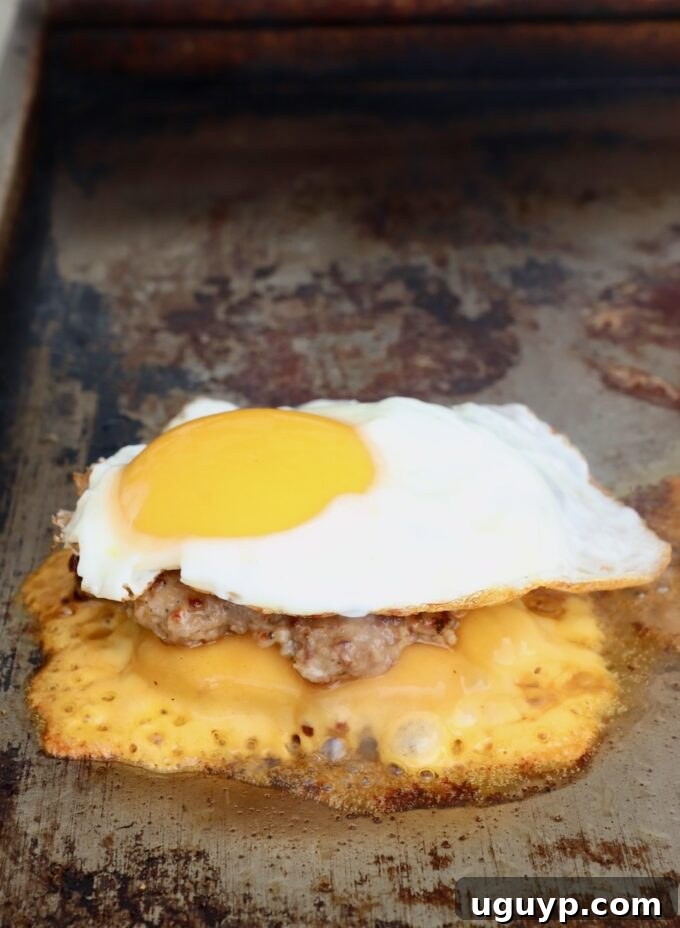 A perfectly fried egg placed on top of a stacked and cheesy smashed burger patty on the griddle.
