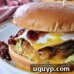 A close-up of a breakfast burger on a plate, topped with a fried egg and glistening bacon jam, ready to be eaten.
