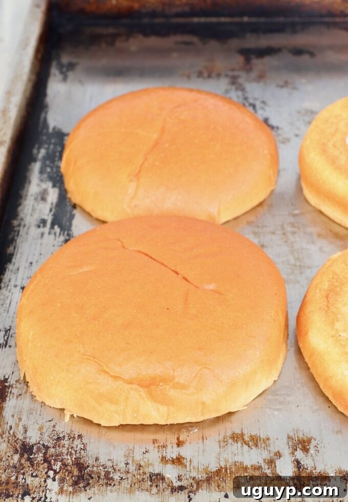 Hamburger buns toasting face-down on a hot griddle, acquiring a golden-brown crisp.