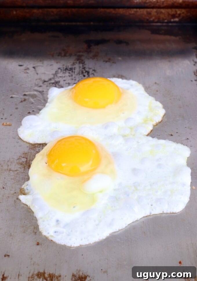 Four eggs perfectly frying on a griddle, their whites setting beautifully.