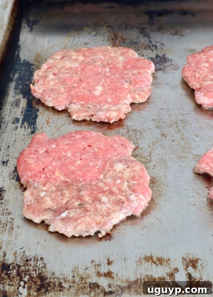 Balls of meat being smashed onto a hot flat top with a metal spatula, forming thin burger patties.