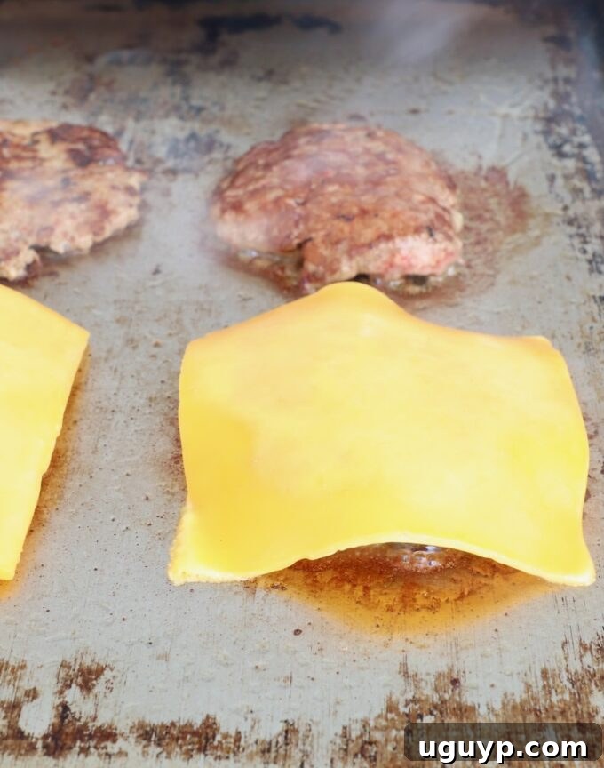 Slices of cheddar cheese carefully placed on half of the cooked burger patties on the hot griddle.