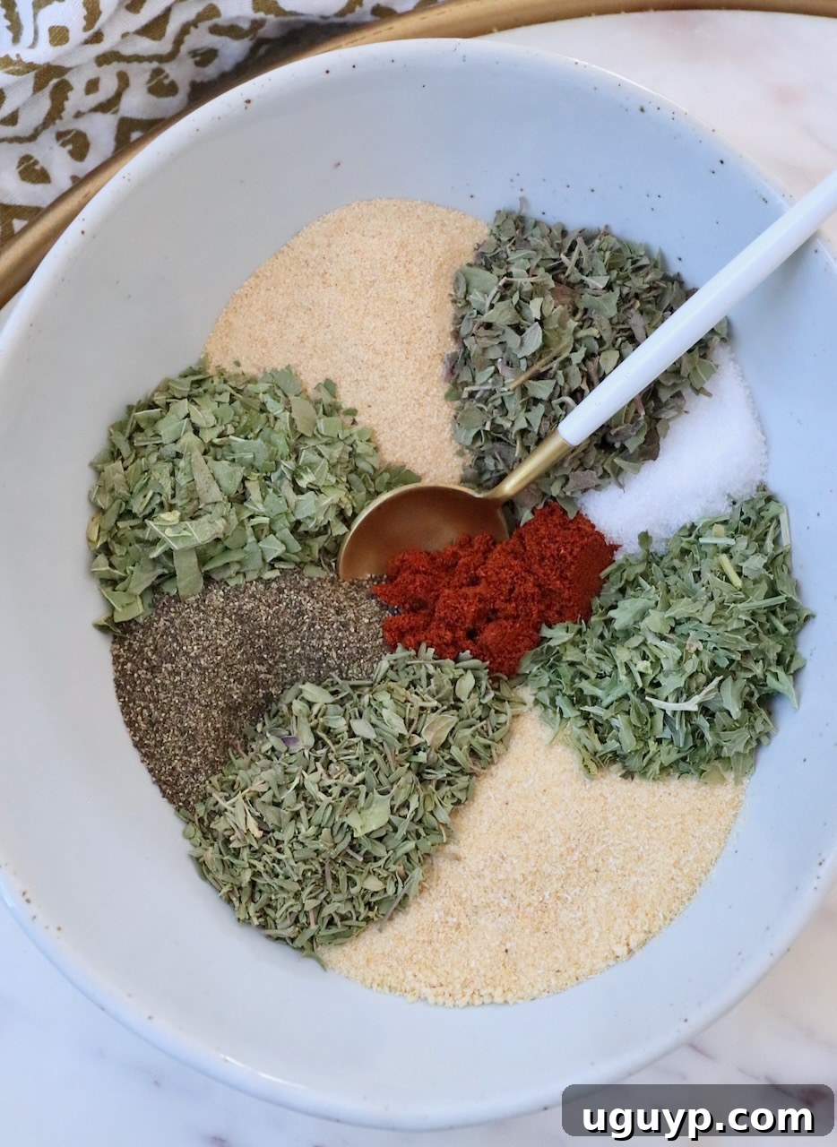 dried herbs and spices separated in a bowl with a spoon, ready to be mixed into a homemade vegetable seasoning