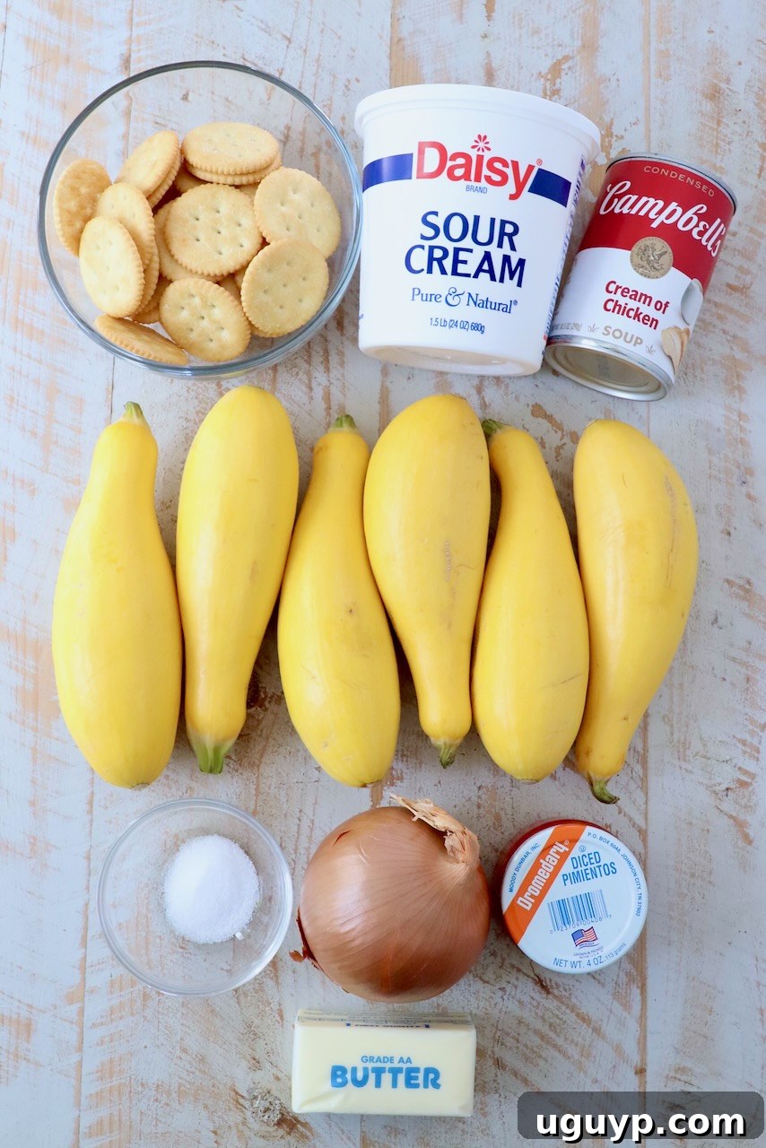 Assortment of fresh ingredients for squash casserole, including yellow squash, onions, butter, sour cream, pimentos, and Ritz crackers, arranged on a white wooden board.
