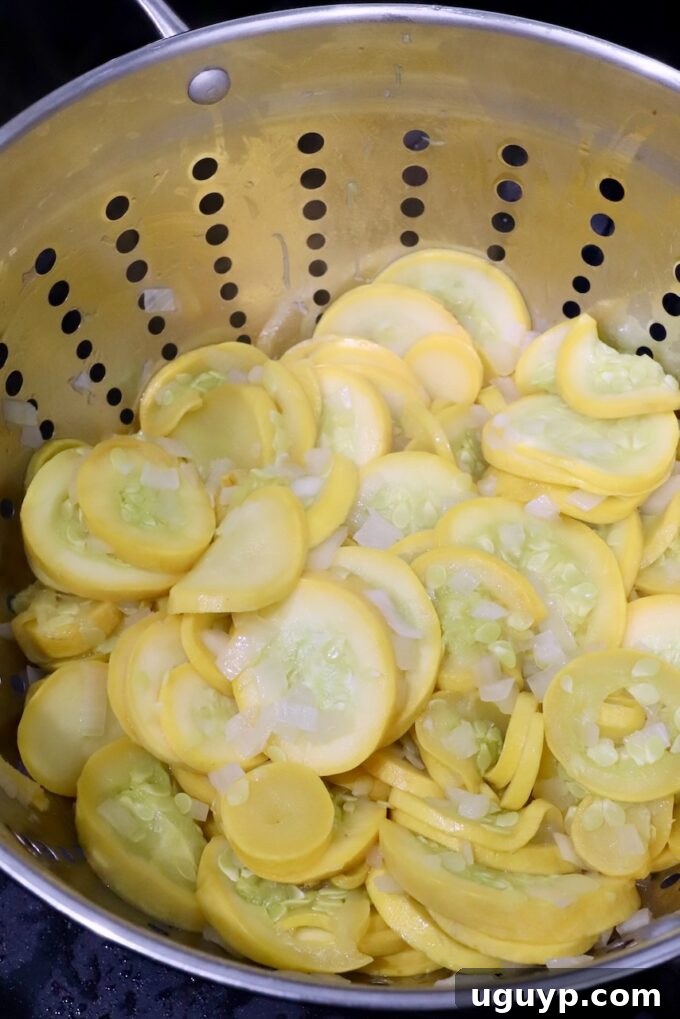 Cooked yellow squash and onions draining in a colander in the sink.