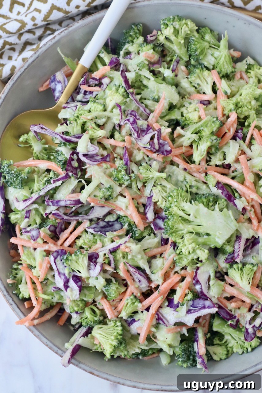 A beautifully presented bowl of creamy broccoli slaw with a serving spoon, emphasizing its freshness and inviting texture.
