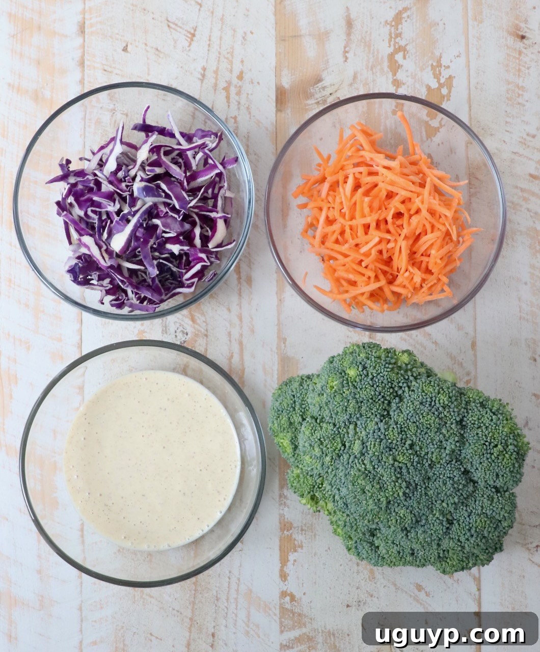 A selection of fresh ingredients for broccoli slaw arranged artfully on a white wooden board.