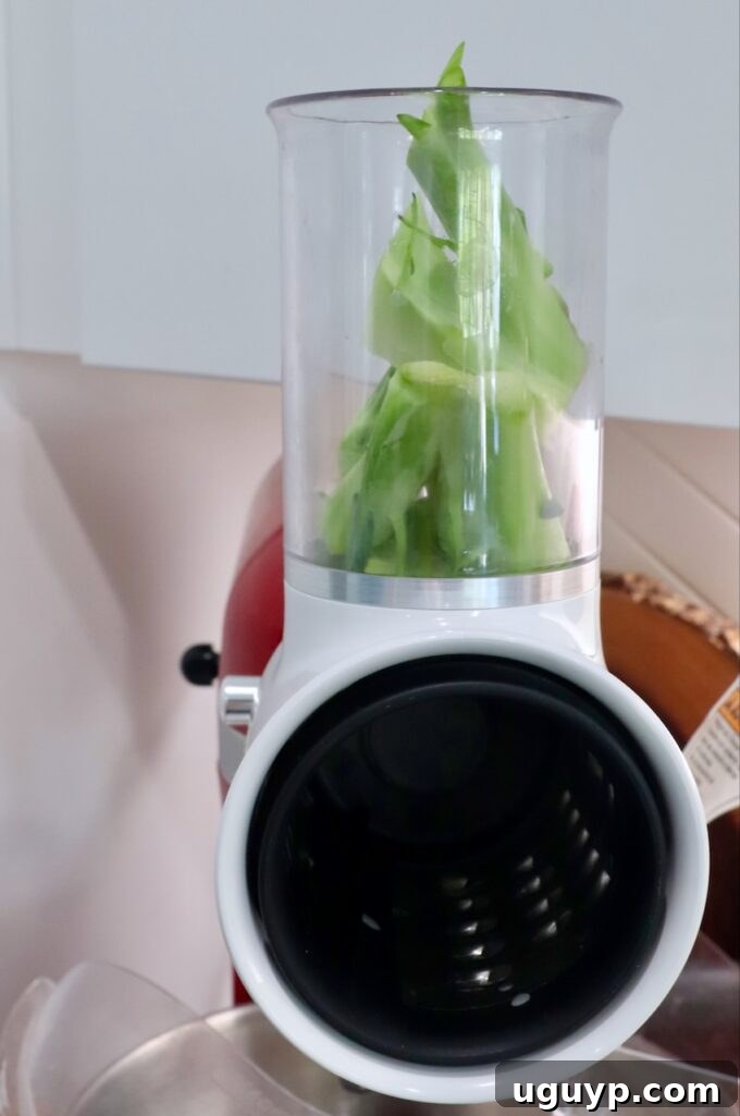 Broccoli stems being shredded using a shredder attachment on a KitchenAid stand mixer.