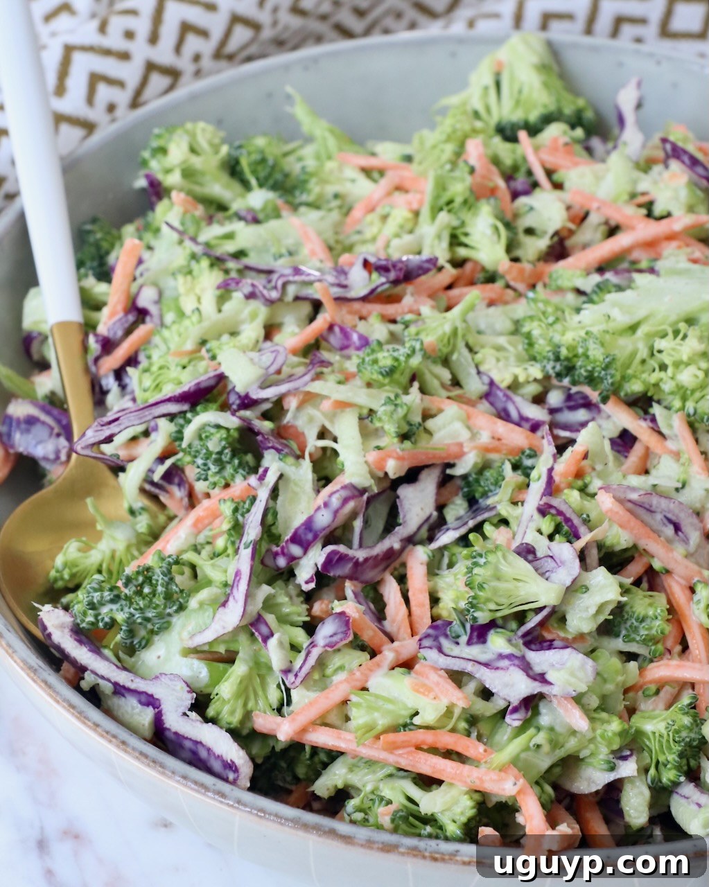 A close-up shot of the finished broccoli slaw in a bowl, showing its creamy texture and fresh ingredients, with a spoon nestled in.