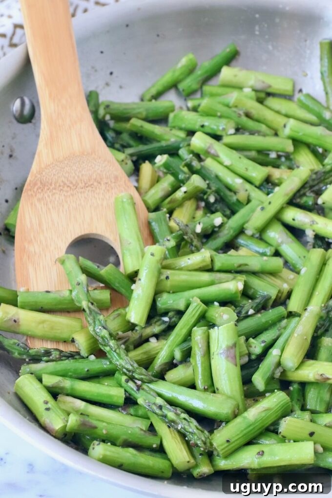 Cooked asparagus pieces in a skillet with a serving spoon, ready to be served.