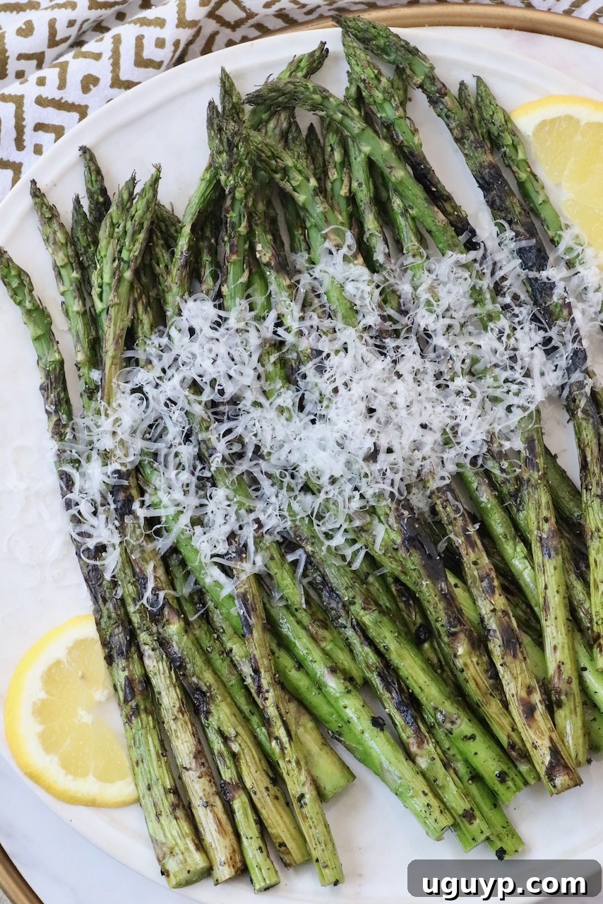 Grilled asparagus topped generously with freshly grated Parmesan cheese on a plate.