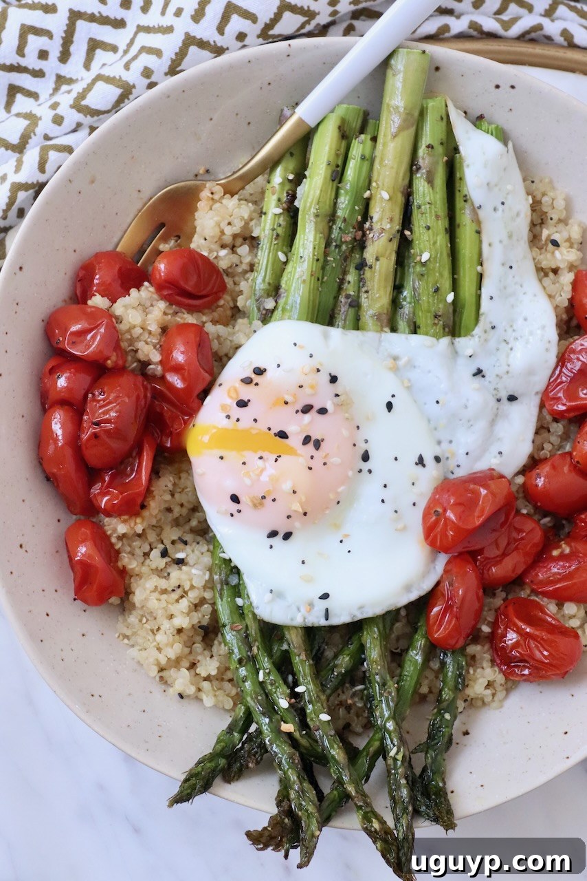 A healthy bowl featuring cooked asparagus, roasted tomatoes, quinoa, and a fried egg.