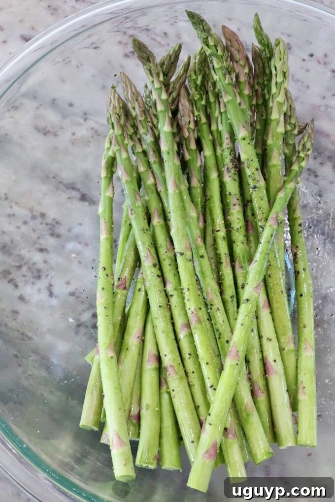 Asparagus spears seasoned with olive oil, salt, and pepper in a glass bowl.