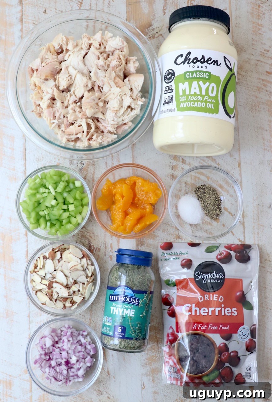 All fresh ingredients for making a vibrant chicken salad laid out neatly on a white wooden board.
