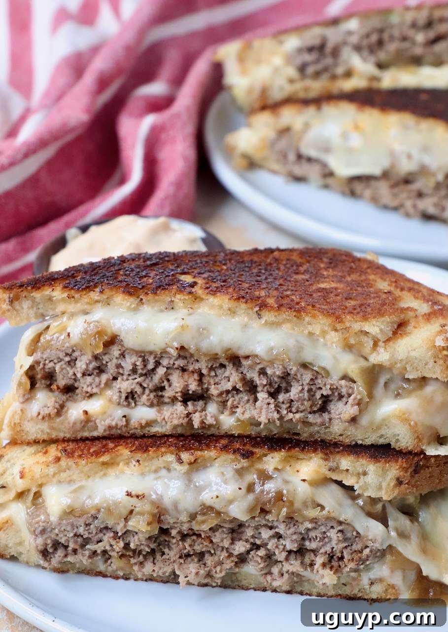 Two halves of a classic patty melt sandwich stacked on a plate, showcasing melted cheese, caramelized onions, and a juicy beef patty.