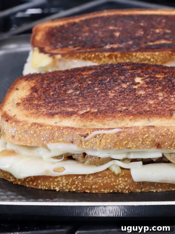 A perfectly golden-brown, cooked patty melt on a griddle pan on the stove, cheese visibly melted.