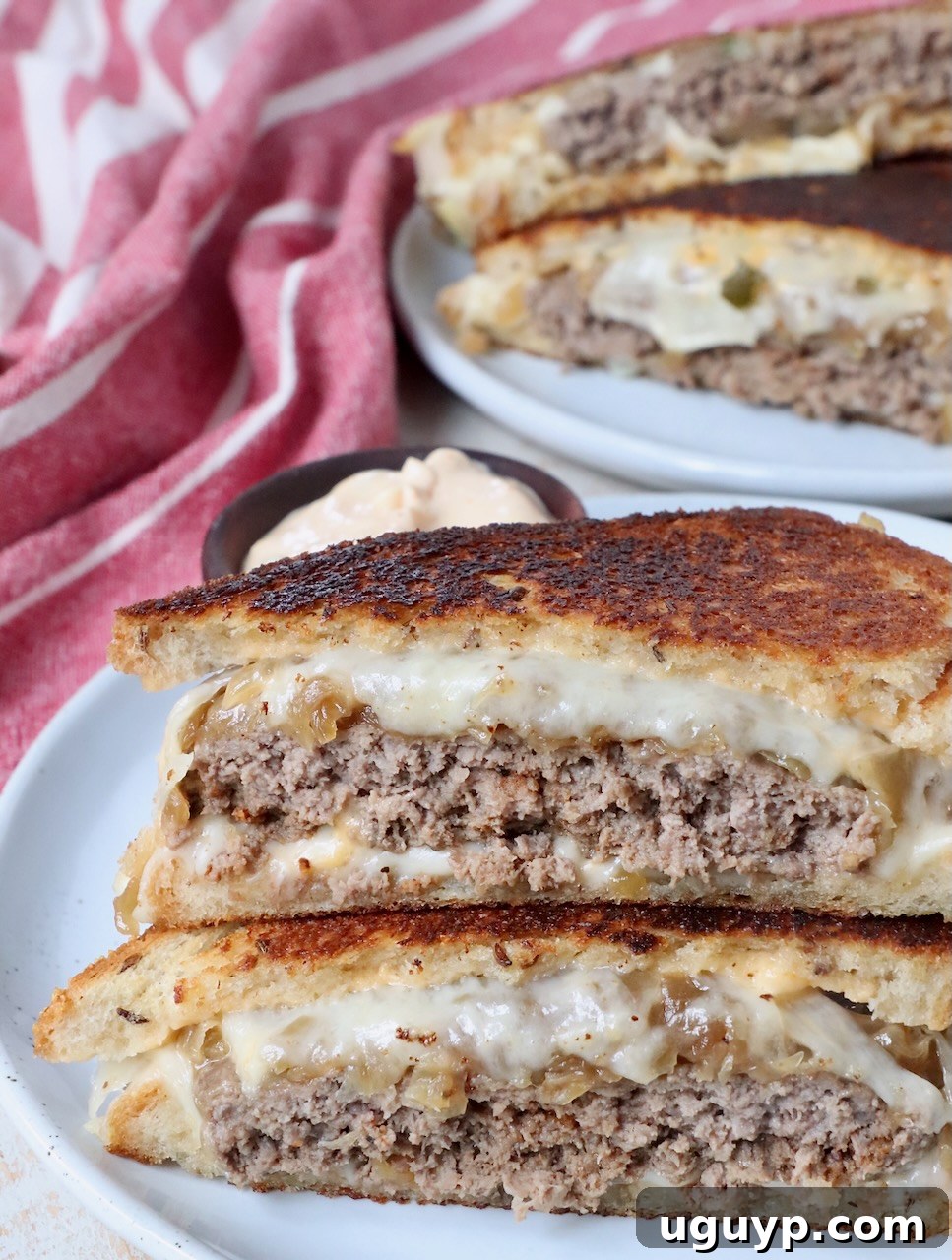 A perfectly cooked patty melt, sliced in half and served on a plate, ready to be eaten.