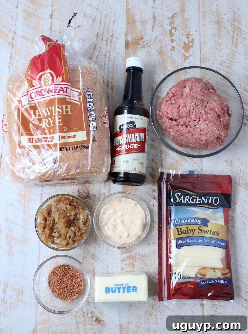 All the fresh ingredients for a homemade patty melt laid out on a white wooden board, including bread, cheese, beef, and onions.