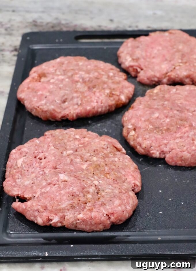 Seasoned raw burger patties on a cutting board, ready for grilling.
