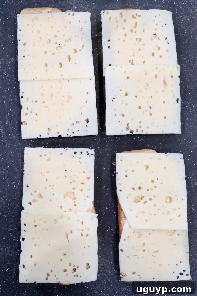 Slices of rye bread topped with Swiss cheese on a cutting board, ready for assembly.