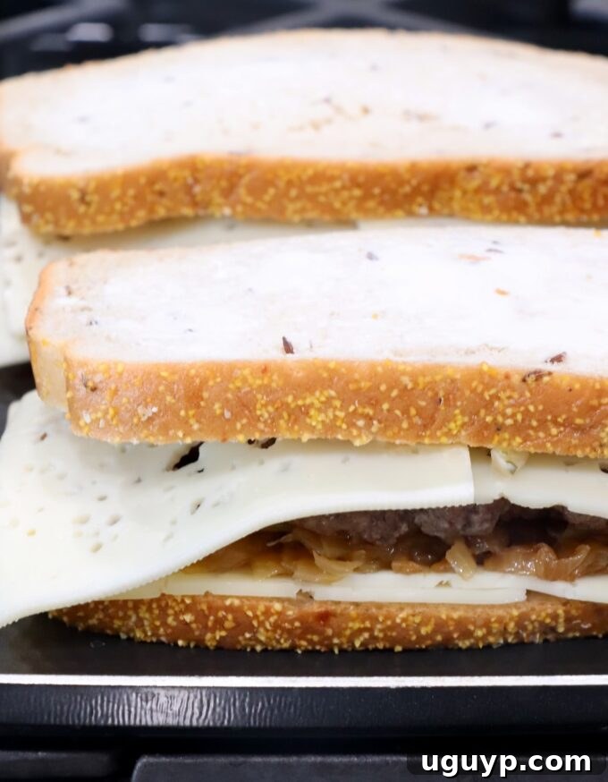 An uncooked patty melt sandwich cooking on a griddle pan, waiting to be flipped.