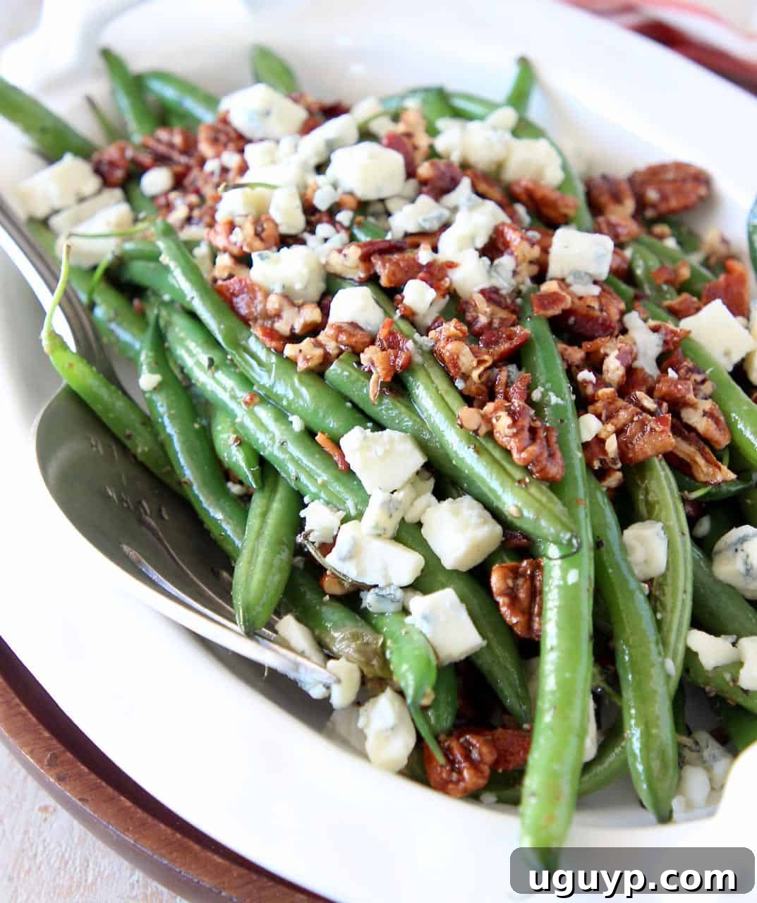 Fresh cooked green beans in serving bowl topped with crumbled bacon, pecans and blue cheese