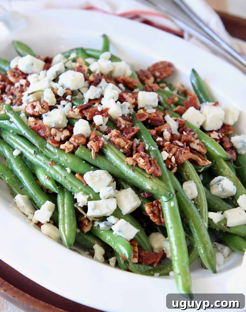 Fresh green beans in serving bowl, topped with pecans and blue cheese crumbles