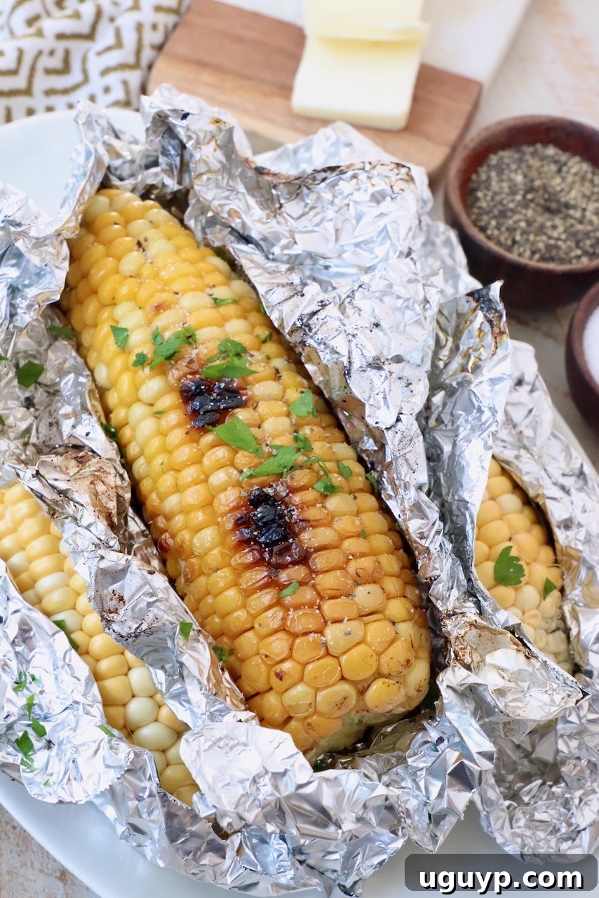 Grilled corn on the cob in foil on a marble platter, ready to be unwrapped and enjoyed.