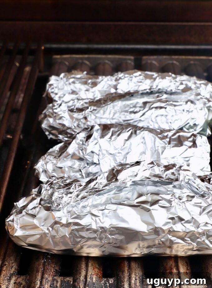 Foil-wrapped corn on the cob cooking on a hot grill.