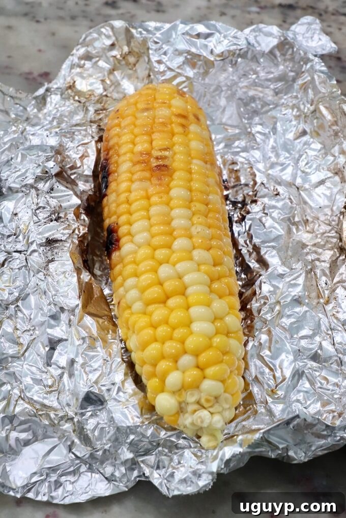 Grilled corn on the cob, still in its foil wrapping, showing slight char marks.