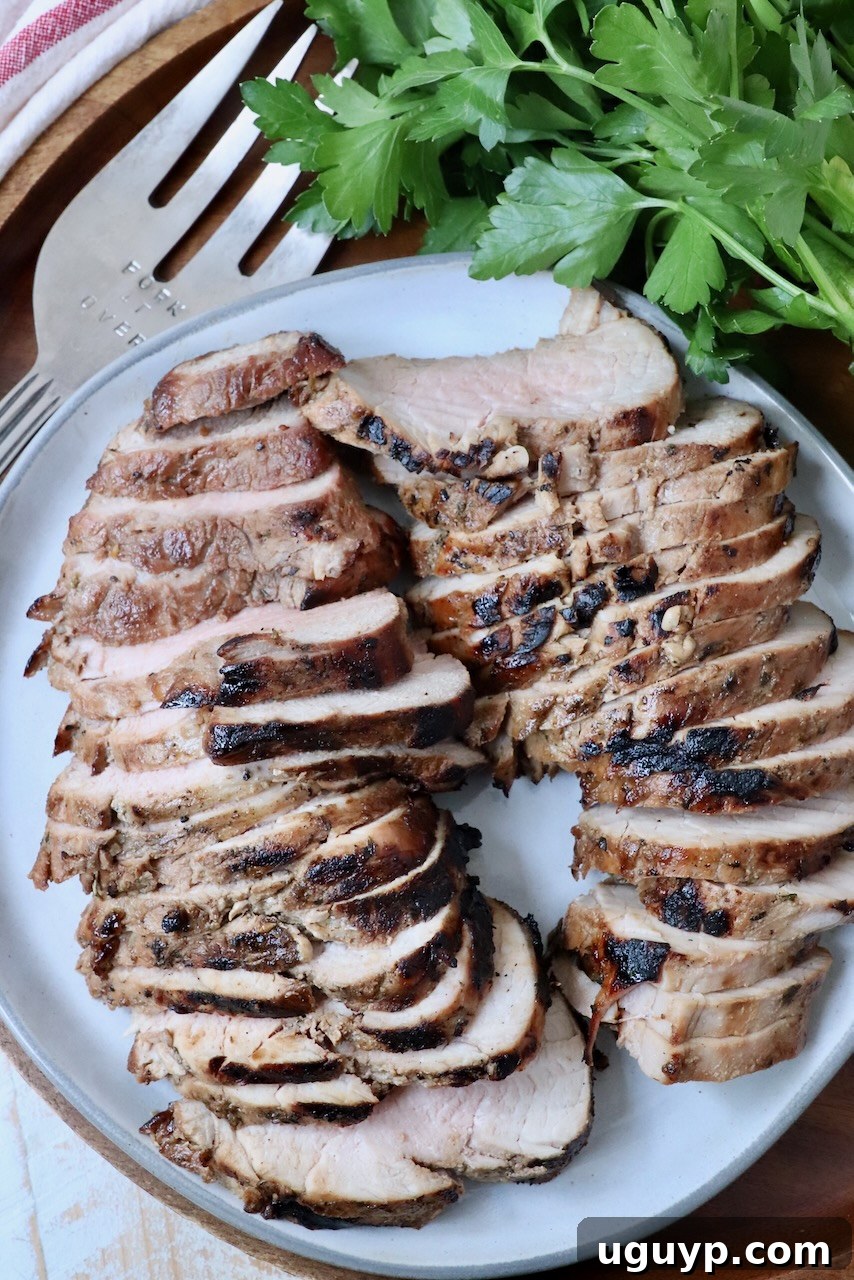 Perfectly sliced, juicy pork tenderloin on a plate, garnished with fresh parsley and a serving fork