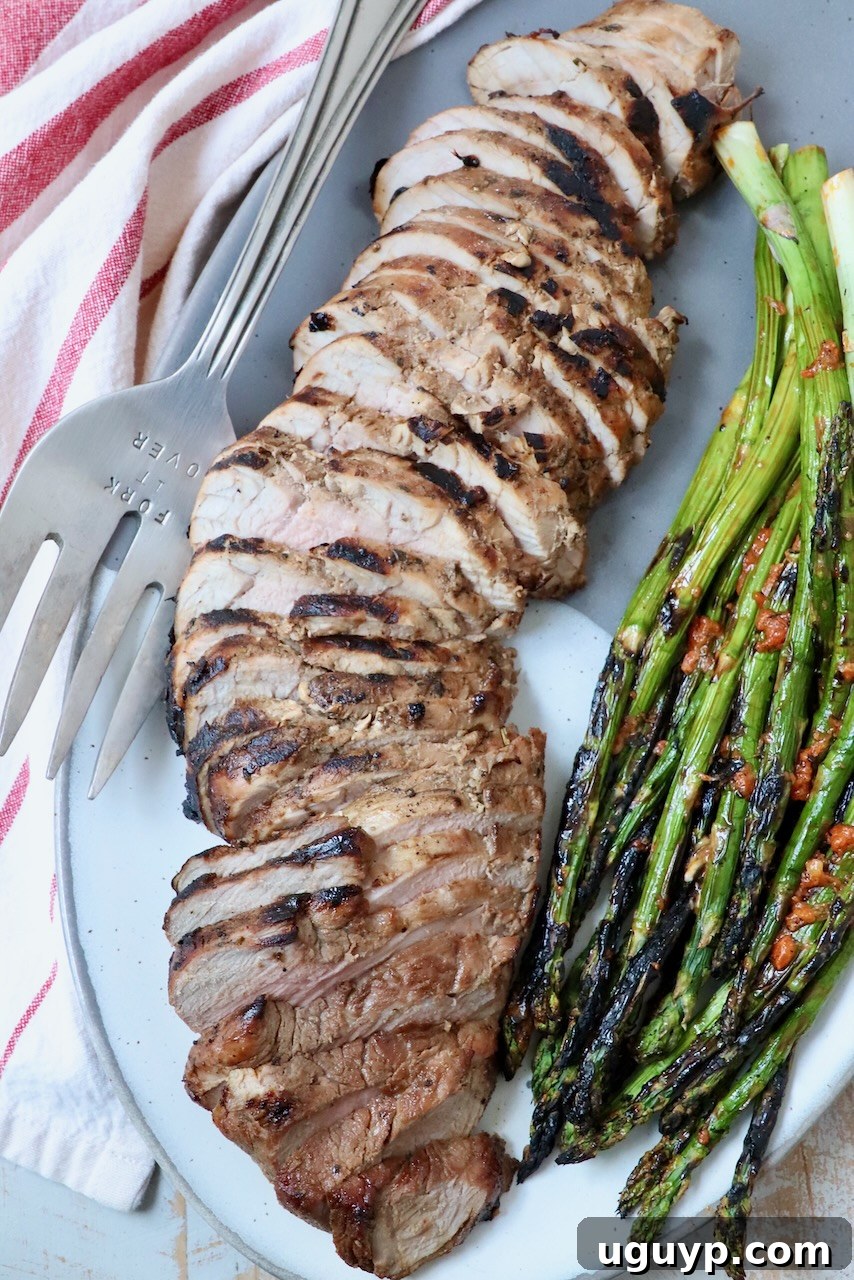 Beautifully sliced grilled pork tenderloin served on a plate with grilled asparagus