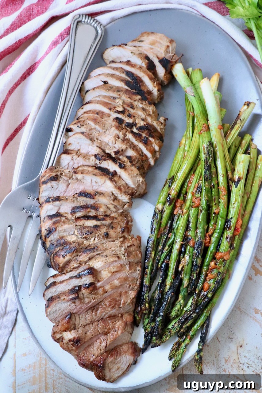 Sliced pork tenderloin with grilled asparagus on a serving plate