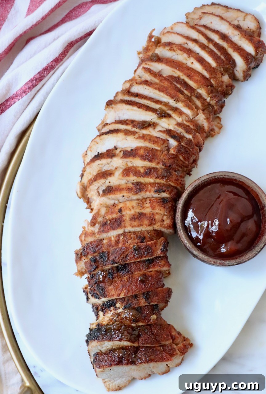 Sliced grilled pork tenderloin on a plate with a small bowl of BBQ sauce on the side.