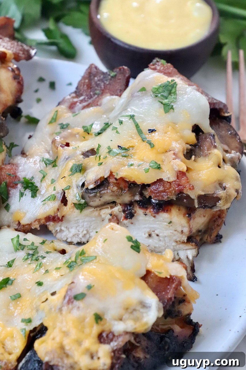Grilled chicken topped with crispy bacon and melted cheese, expertly sliced in half on a pristine white plate, ready to be served.