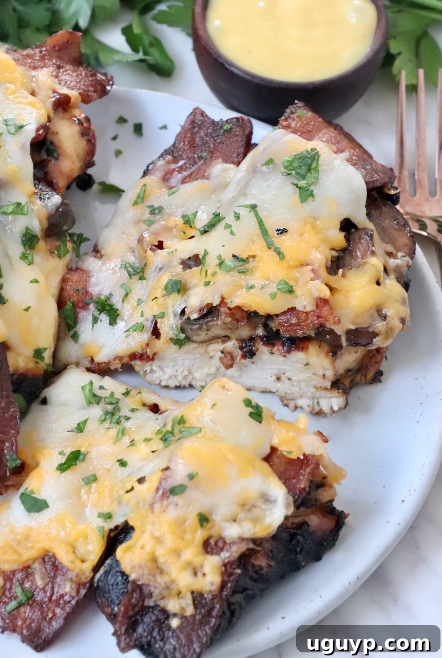 A close-up shot of grilled chicken topped with bacon and melted cheese, sliced in half, presenting a mouthwatering view on a white plate.
