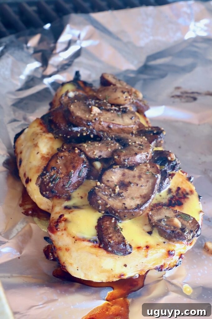 Grilled chicken topped with savory sautéed mushrooms, carefully arranged on foil inside a grill.